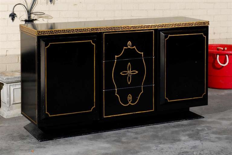 1960's Hollywood Regency black lacquer credenza with gilt greek key detail banded along the top edge.  A gilt frame accents each side of the cabinet, the three center cabinet drawers, and runs along the canted edges of the cabinet doors.  A