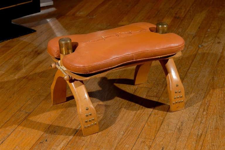 20th Century Camel Saddle Stool from Egypt, made of wood with brass etched details and brass tacking, and seat of orange faux leather and stitched decorations.
