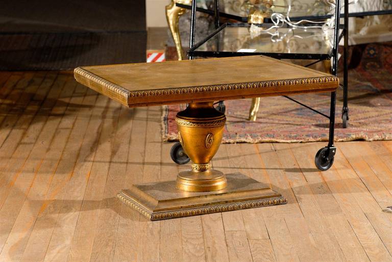 Pair of Hollywood Regency decorative urn shaped side tables on pedestal bases with inset gold leafed tops and egg and dart carved moldings around the perimeter of the tops and bases.  Perfect for cocktail tables or place side by side for a coffee