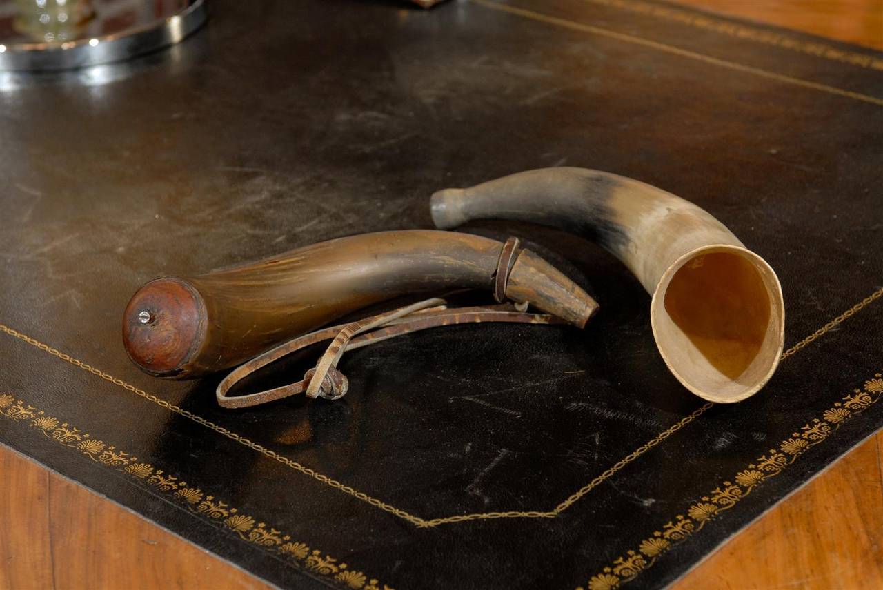 An antique black powder horn with leather handle and a larger fox horn.