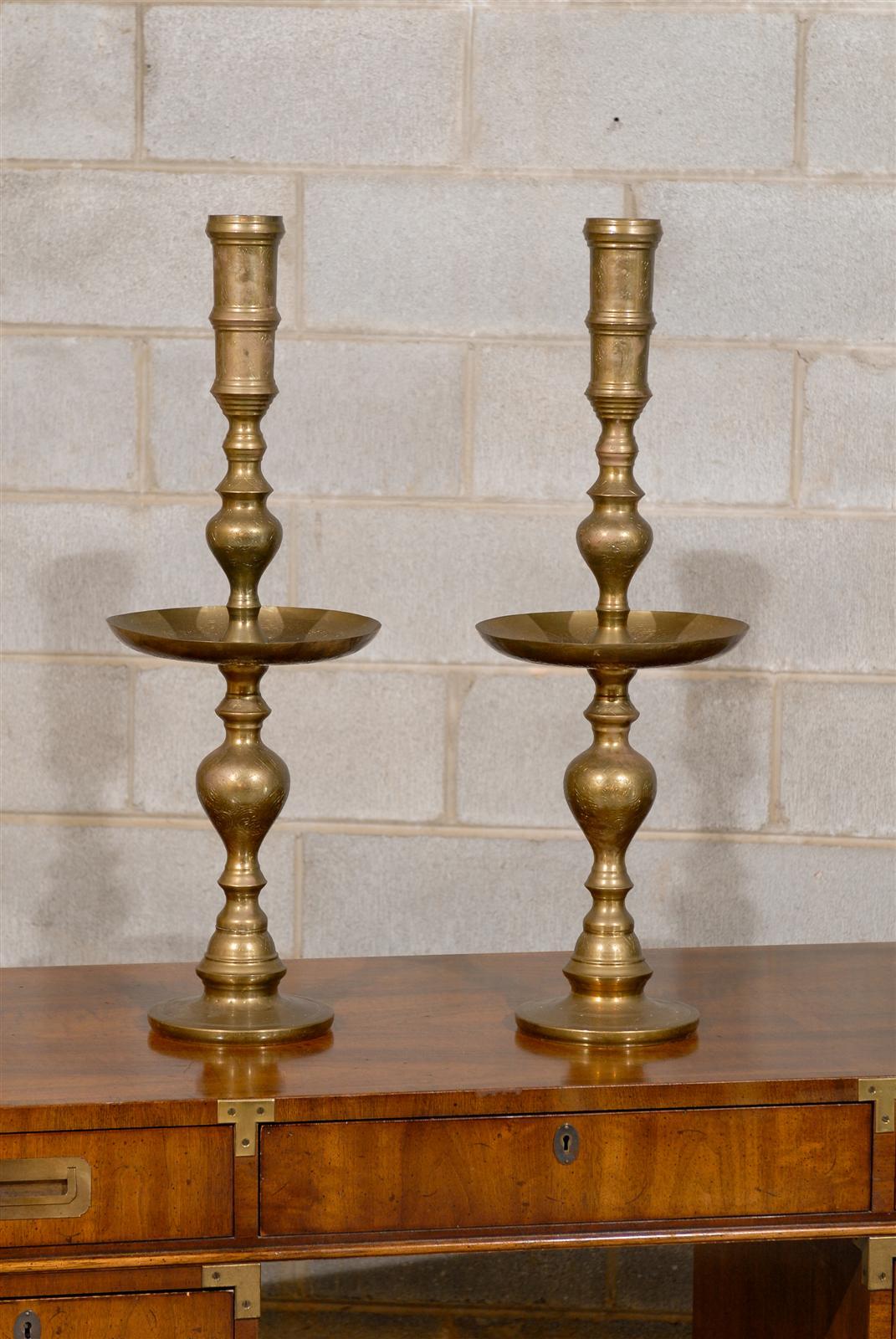 Mid-20th century tall pair of candlesticks of brass and having oversized drip pans.  Made in and stamped Thailand.