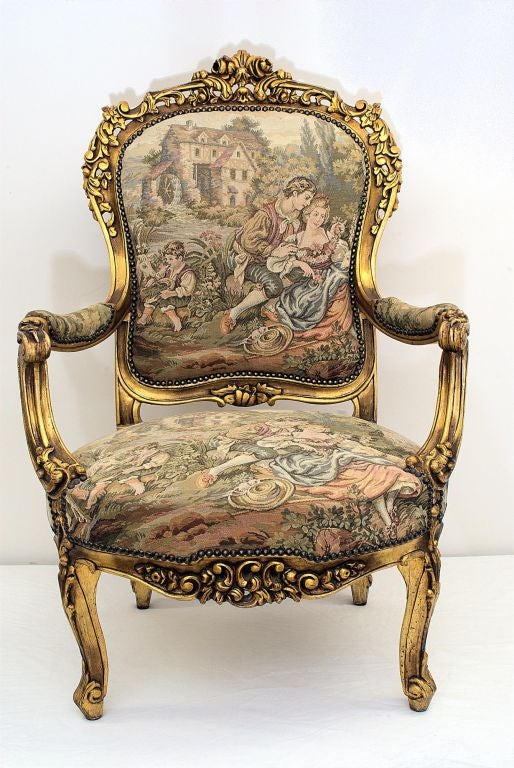 Two Giltwood Fauteuils in the Louis XV Manner with French Gobelin Fabric. The French Gobelin style tapestry scene on this pair of matching armchairs depicts a water mill, a courting couple, a sheep, and a young boy with a pet goat. Carved fruits and