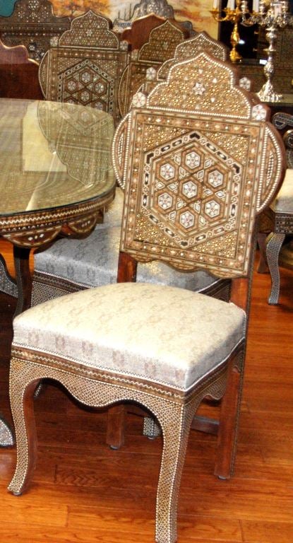 Syrian Inlaid Mother-of-Pearl Dining Chair. This chair is mother of pearl and wooden mosaic inlay with a shaped cornice and apron. The seat of the chair is in a crème colored fabric with blue and gold embellishments. (7 available)
