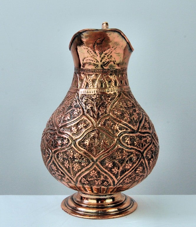 Persian Copper Pitcher. Embossed floral motifs over a bulbous body. Scrolled handle.
