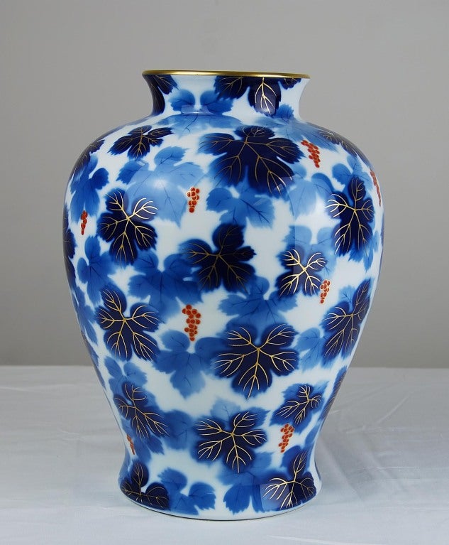 Japanese Porcelain Vase by Fukagawa. An urn-form vase decorated with two-tone blue and gilt leaves and red berries on a white ground. Gilt rim. Marked on the underside with the silver and blue Fukagawa foil label reading
