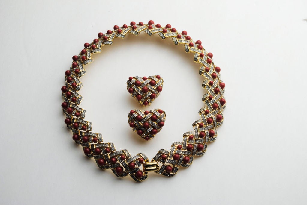 The choker necklace consists of twenty-six sequentially attached heart forms, each decorated with three rust colored cabochon beads surrounded by rectangular panels of tiny encrusted crystals simulating diamonds. The matching earrings are similarly