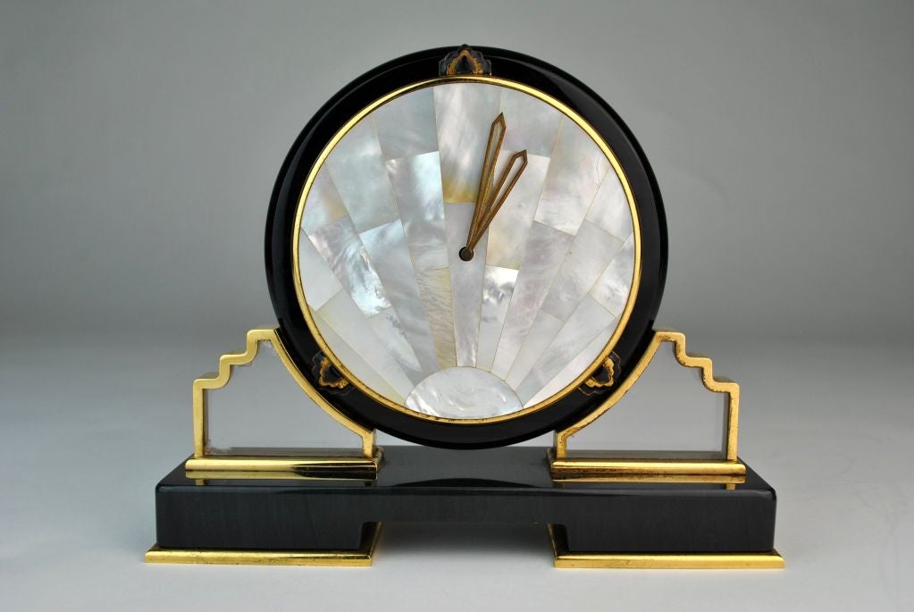 Cartier Desk Clock in the Art Deco Style. Circa 1980’s. A black hardstone, gilt-metal, rock crystal, and mother-of-pearl desk clock by Cartier. Circular case flanked by two rock crystal inserts surrounded by a stepped gold frame. Geometric black and