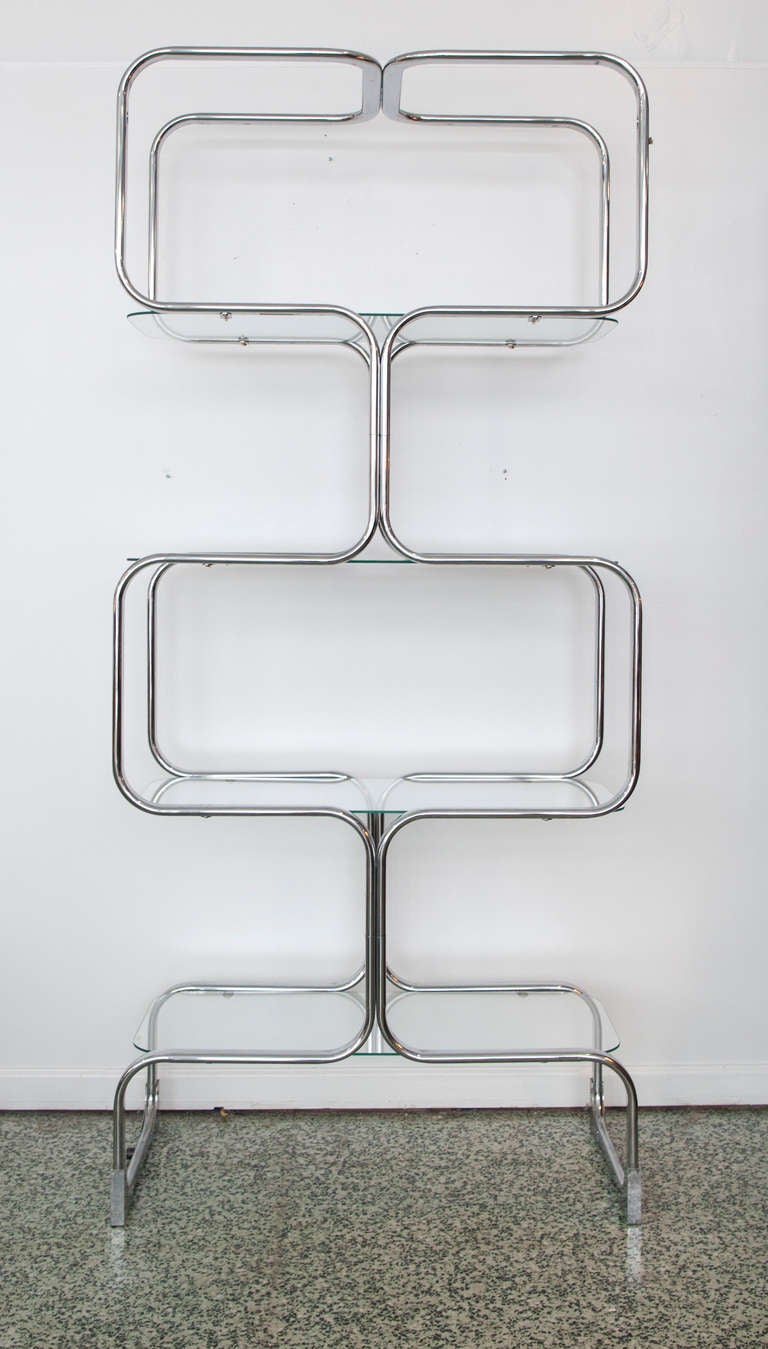 Fabulous pair of Italian chrome and glass etageres constructed of bent metal sections, with glass shelves and radiused corners. Manufactured by Italian furniture company Tricom. In the style of Milo Baughman.