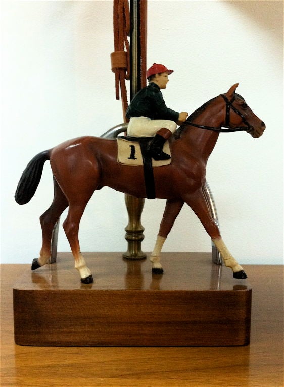 American 1940s painted metal table lamp with jockey figure on horse on ebonized square wood base with horseshoe finial and leather strap post.