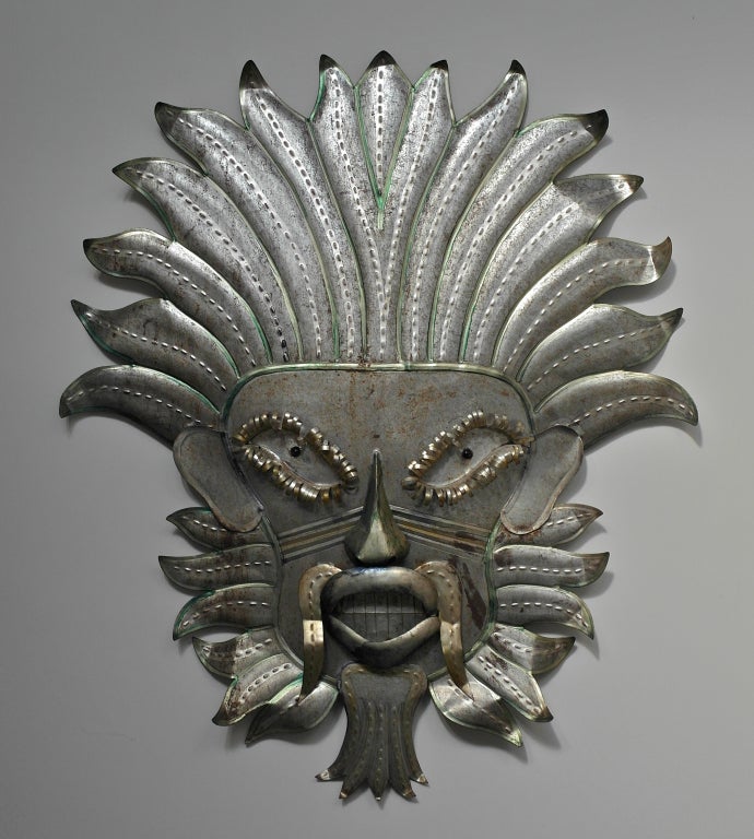 A large tin mask with faded paint decoration.