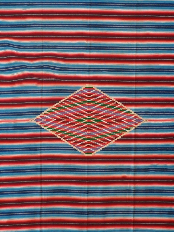 Porfiriato period serape finely woven with a large central diamond combining the colors of the mexican and french flags. The diamond floats on a field of red with and blue stripes symbolizing the strong influence of the French on Porfiriato Mexico