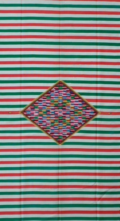 Centennial serape with a large multi colored pulsating central diamond floeating on a ground of red, white and green, the colors of the mexican flag. The central diamond is framed in a border of polychrome arrows. The pieces is possibly from San