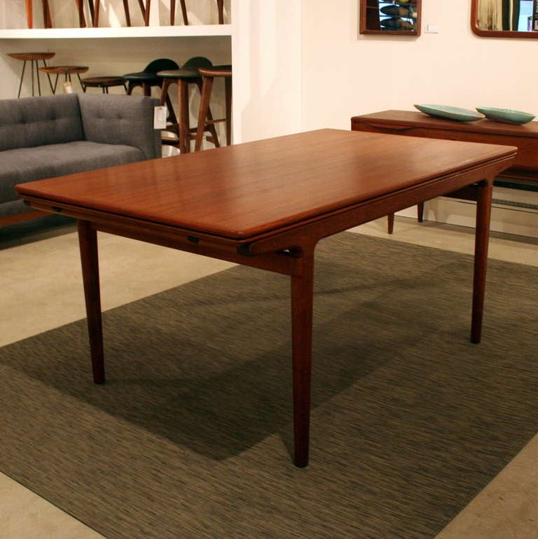 A sleek and distinctly Danish teak dining table with fluidly shaped, tapering legs, re-finished top surface, and two expansion leaves measuring 19.5