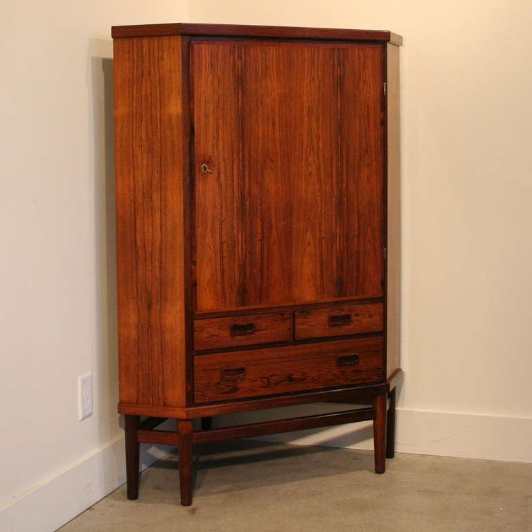 This unique rosewood corner cabinet creates storage space in an area that is usually forgotten. Turned leg base with stringers and darker rosewood edges. Plenty of storage with three fixed shelves and three lower drawers. Complete with the original