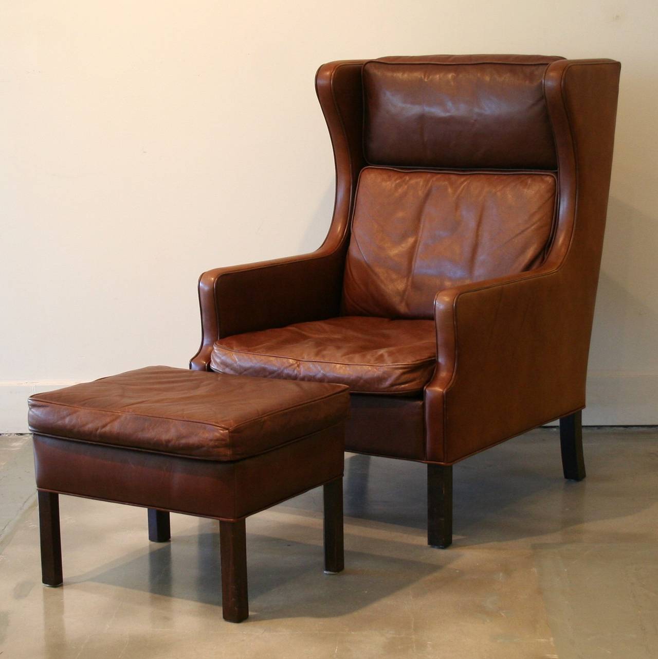 This brown leather wing-back chair is designed in the style of Borge Mogensen, with a gently slanted back and side wings which slope down into the armrests. Cushions have removable covers and are filled with foam and down/feather wrap. This charming