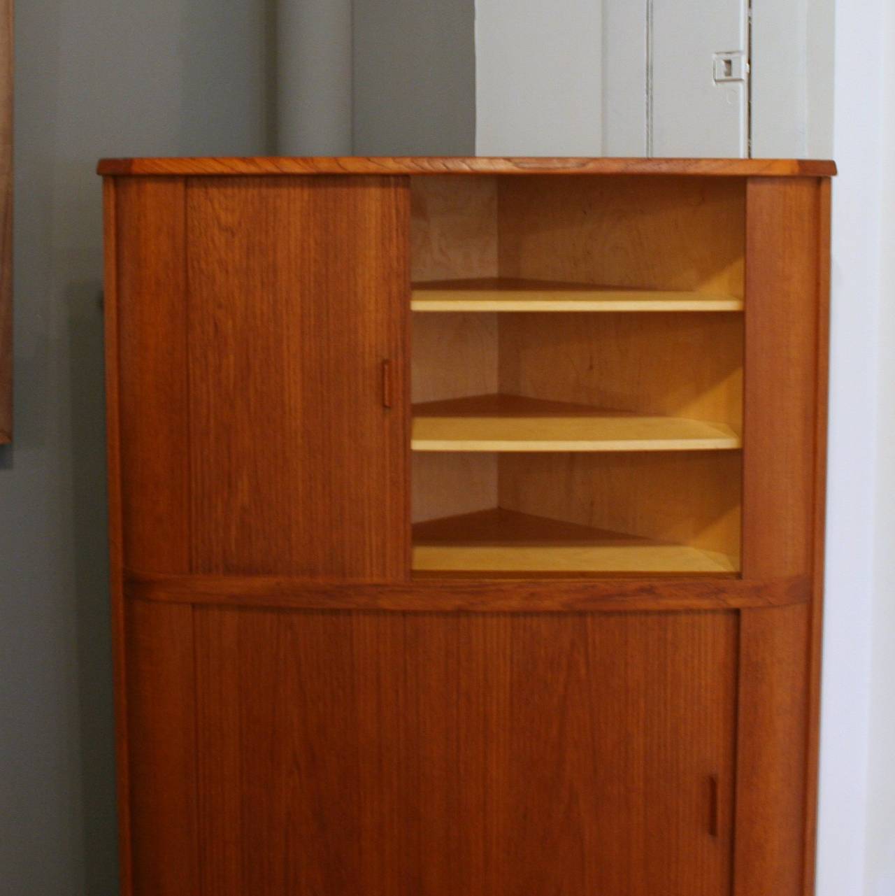 A lovely storage piece for the corner, this cabinet crafted in teak features smooth-gliding tambour doors and a rich wood grain. Supported by solid turned teak legs, with adjustable interior shelving, this piece makes a stunning liquor cabinet or