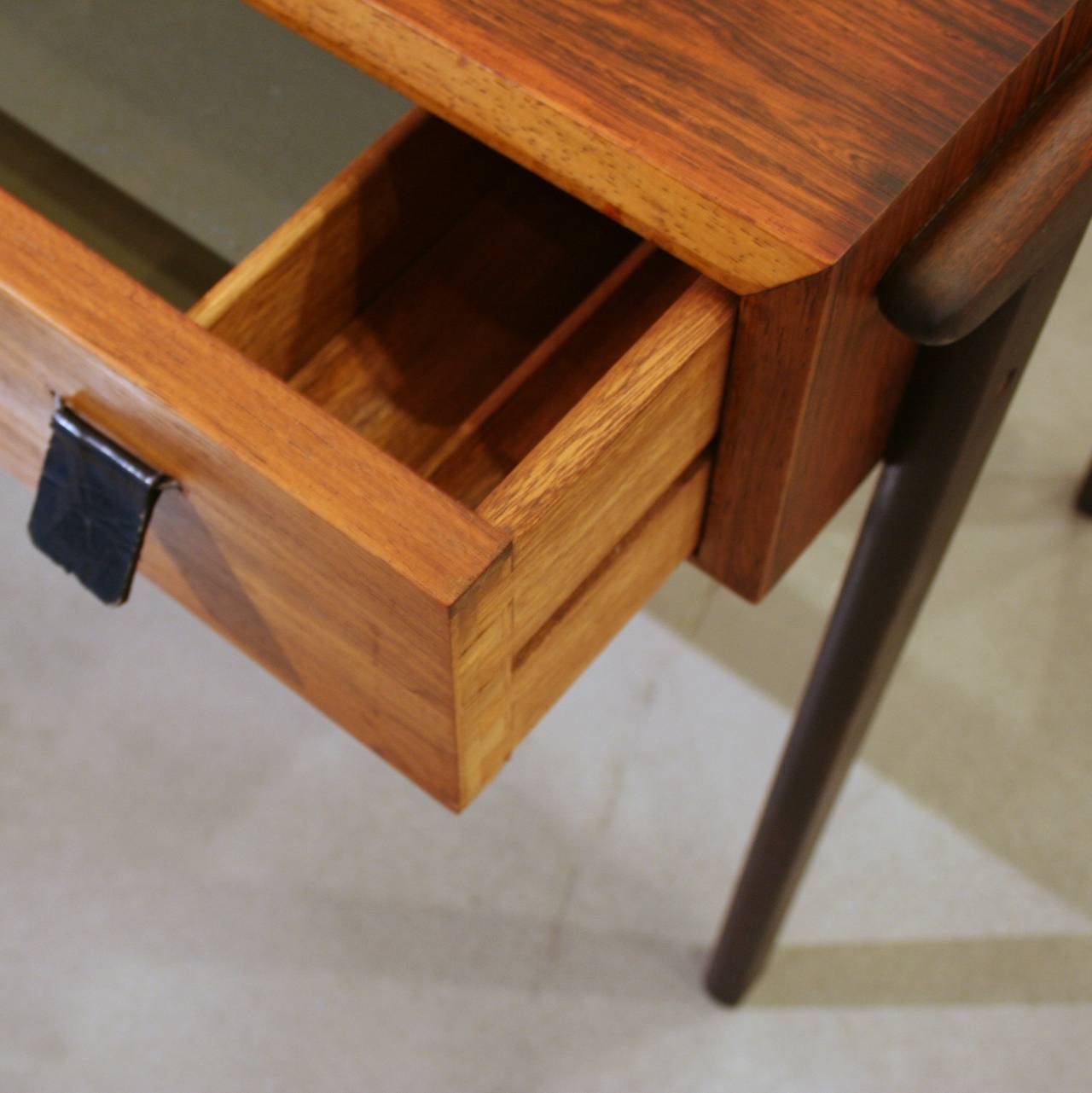 A unique solution for a side table with storage, this piece was originally designed as a sewing table. Featuring a stunning rosewood grain and rich patina, there is also a single drawer with leather tab pulls, and splayed legs which are stained