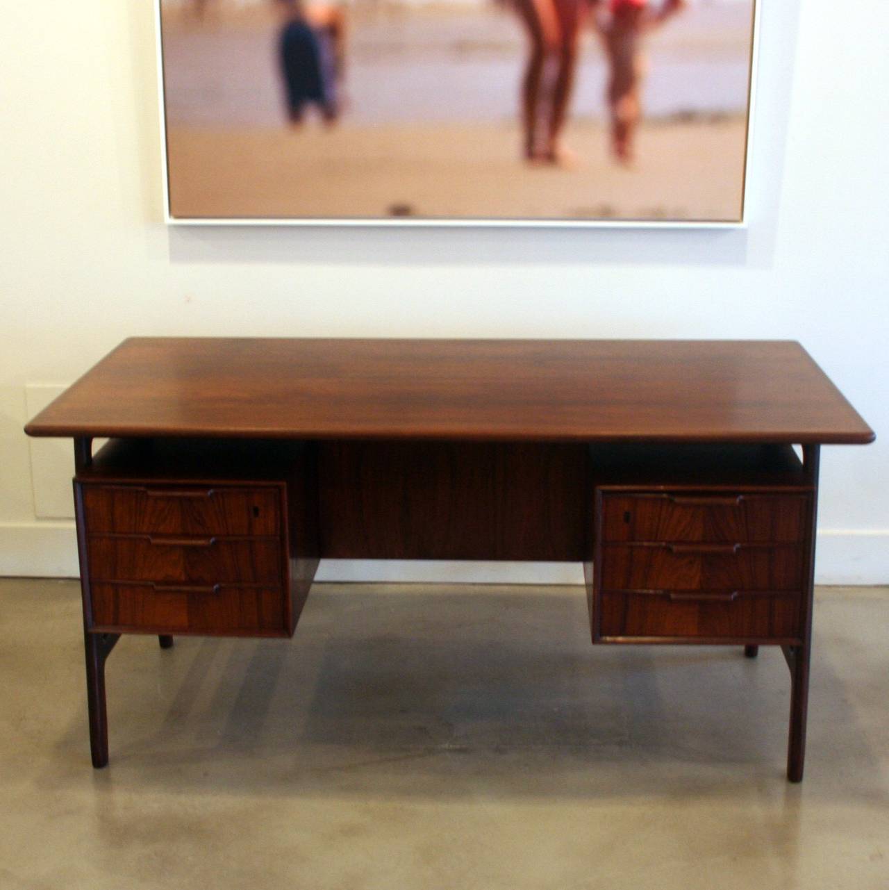Classic Danish desk design masterfully crafted in Brazilian rosewood with sculptural legs framing the double drawer pedestals. Six dove-tailed drawers with curved pulls that fit the hand just right. A rear drop-down cabinet is nestled between cubbie