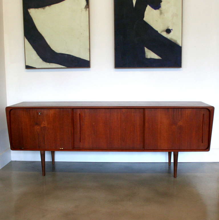 Unique sideboard crafted in teak with two sliding doors and a drop-down cabinet. Etched mirrors are featured in the bar areas on each end and adjustable shelving in the middle. Solid wood conical legs, angled sides with curved lines and antiqued