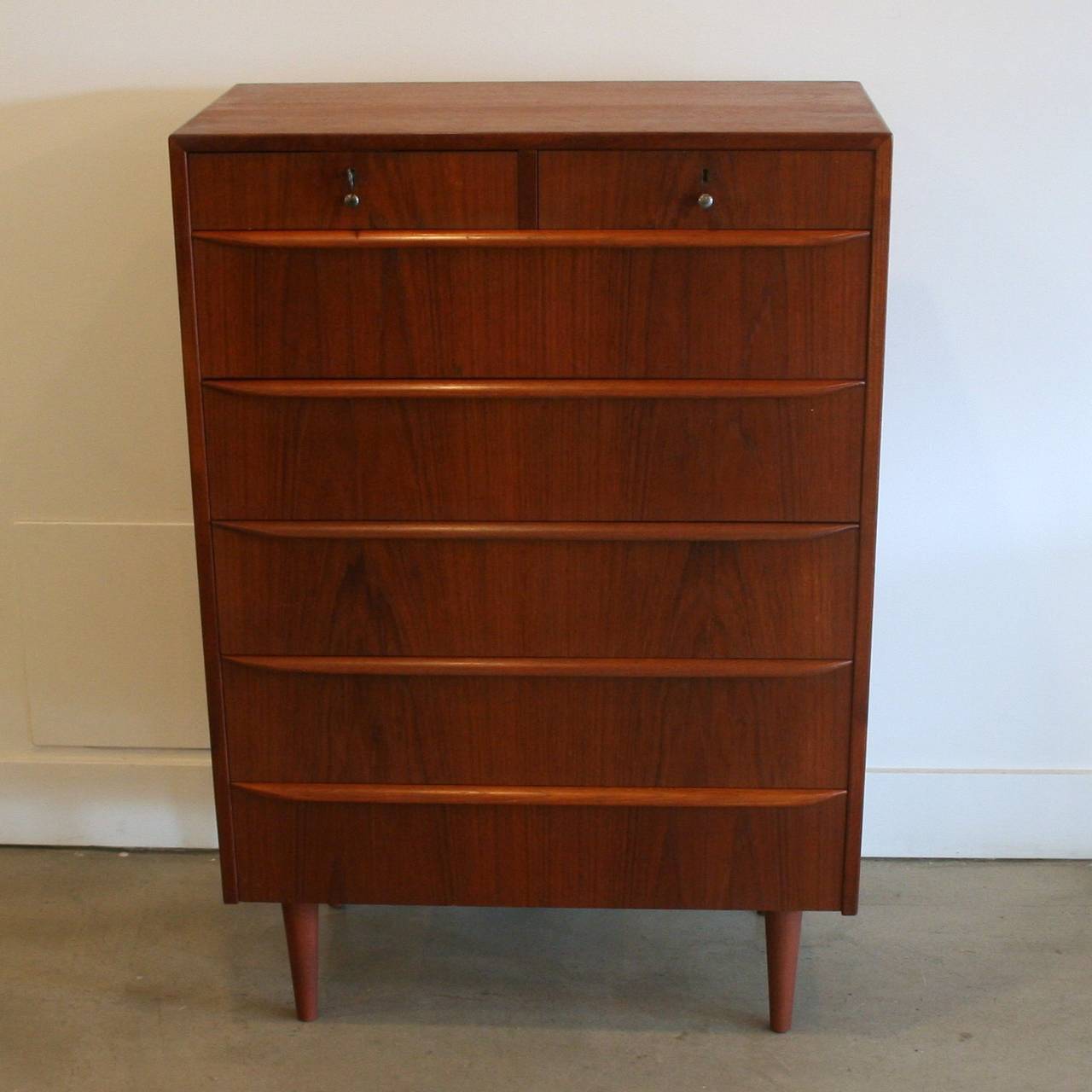 A vintage tallboy with two large small drawers on top of 5 larger bottom drawers. Featuring solid teak pulls and conical legs, dove-tailed drawers, and warm teak character.