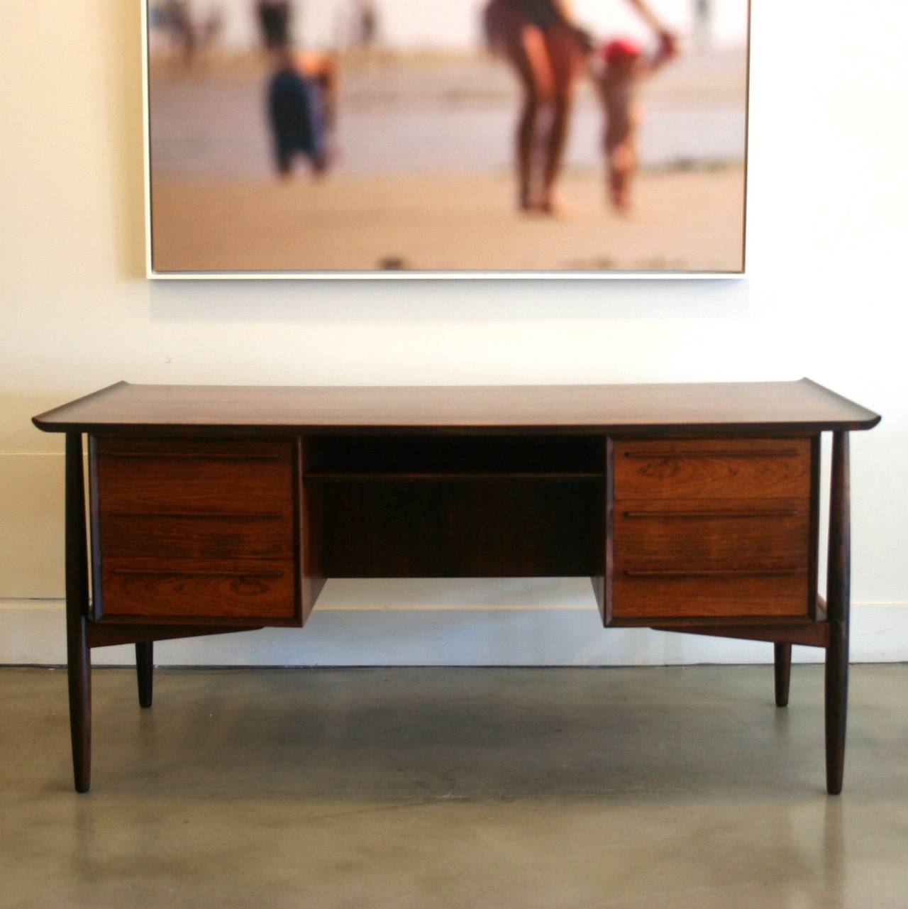 An exquisitely designed Danish modern desk by Gunni Omann with raised-lip edges. This piece features a stunning rosewood grain and rich colour. Framed by solid turned legs, the double bank of drawers feature dove-tailed construction and clean,