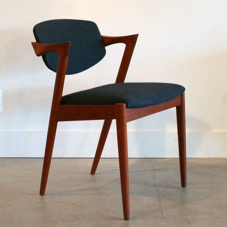 The famous 'tilt-back' chairs by Kai Kristiansen are presented in solid teak with striking angles and subtle curves. Newly upholstered in a contrasting charcoal fabric, this set of four dining chairs are a conversation piece.