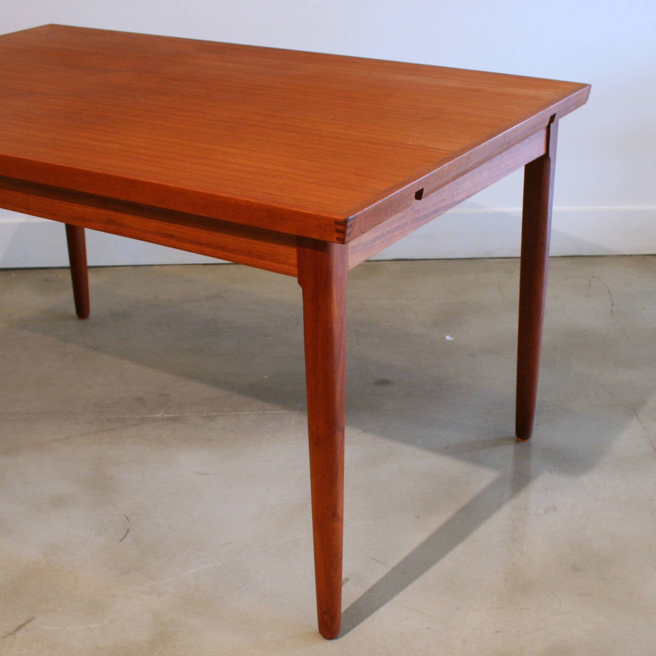 Stunning small scale teak dining table with two hidden leaves. Easy to extend drawer leaves hid under the beveled lip of the table top. Dovetail detailing at the corners. Resting on solid teak legs. Made in Denmark.