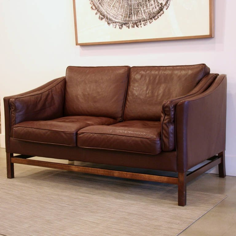 A stunning leather two-seat sofa featuring supple full-grain leather in a wonderful dark plum color. Loose cushions are filled with foam and down or feather wrap. Sloped armrests create a sleek profile and the wooden leg base adds extra detail.