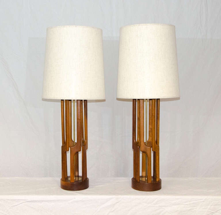 Large pair of Modeline style table lamps with tall architectural wood bases. Brass post accent in the center and brass circular accent on the base. Lamp shades are vintage, 19