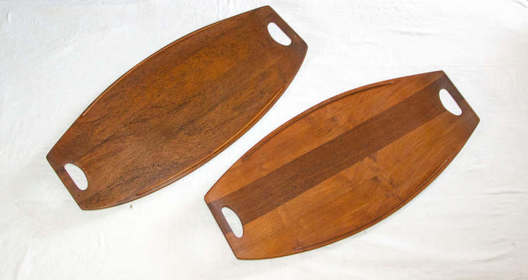 Two large teak serving trays with finger spaces at each end. Dansk, IHQ (Quistgaard) and four ducks logo incised on flip side. Each tray top has small raised rails on both sides & each tray sits on two small raised rails attached to underside to