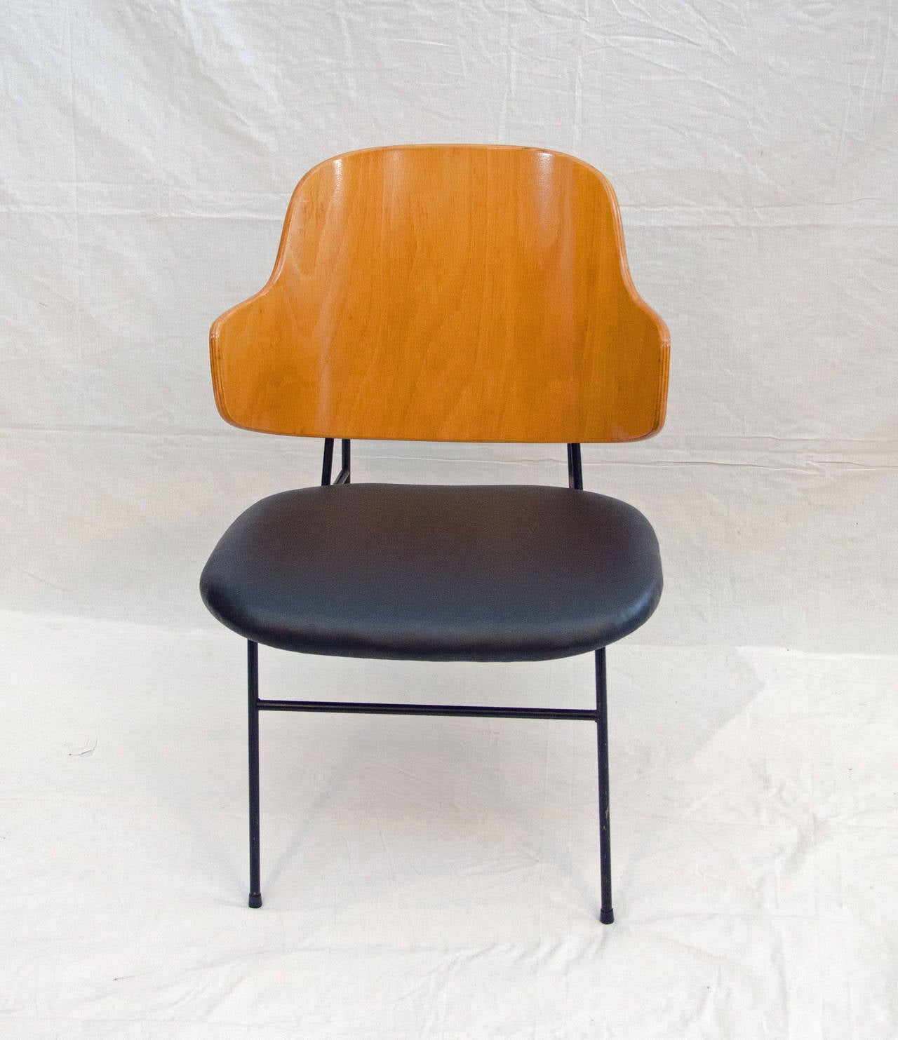 Comfortable smaller scale lounge chair, would be a nice accent for your mid century interior also fits in well with a more industrial  theme. Iron frame supports the bent birch ply curved back and the black vinyl seat.