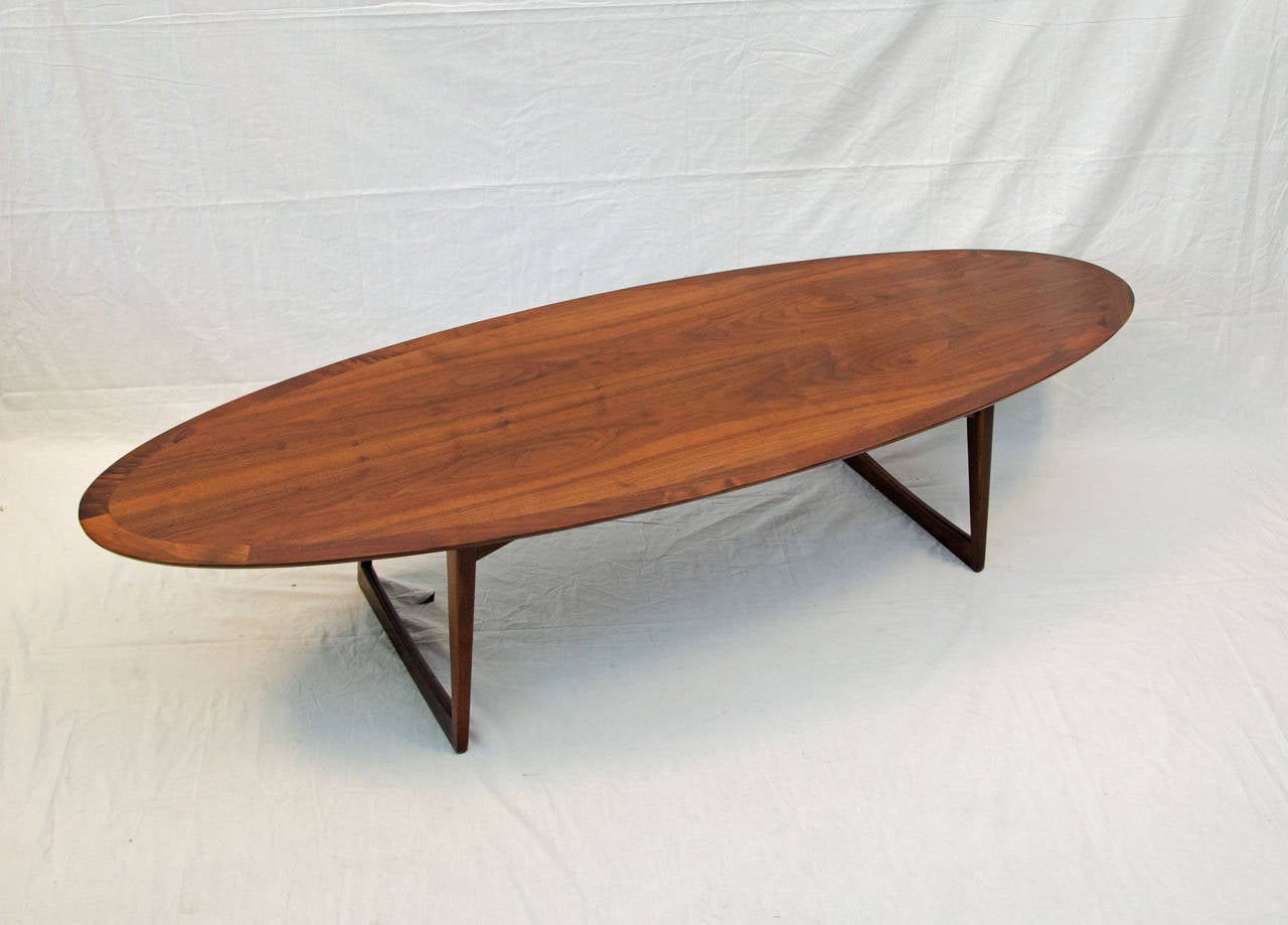 Beautiful surfboard shape walnut coffee table. The table top is supported by two sets of slightly angled legs. The table top is accented by a 1 3/4