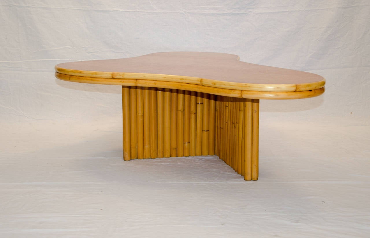 Wonderful free form organic shaped rattan and blonde mahogany coffee table designed by Herb & Shirley Ritts for Ritts Tropitan. Tabletop has rattan trim atound the edges and is supported by a 