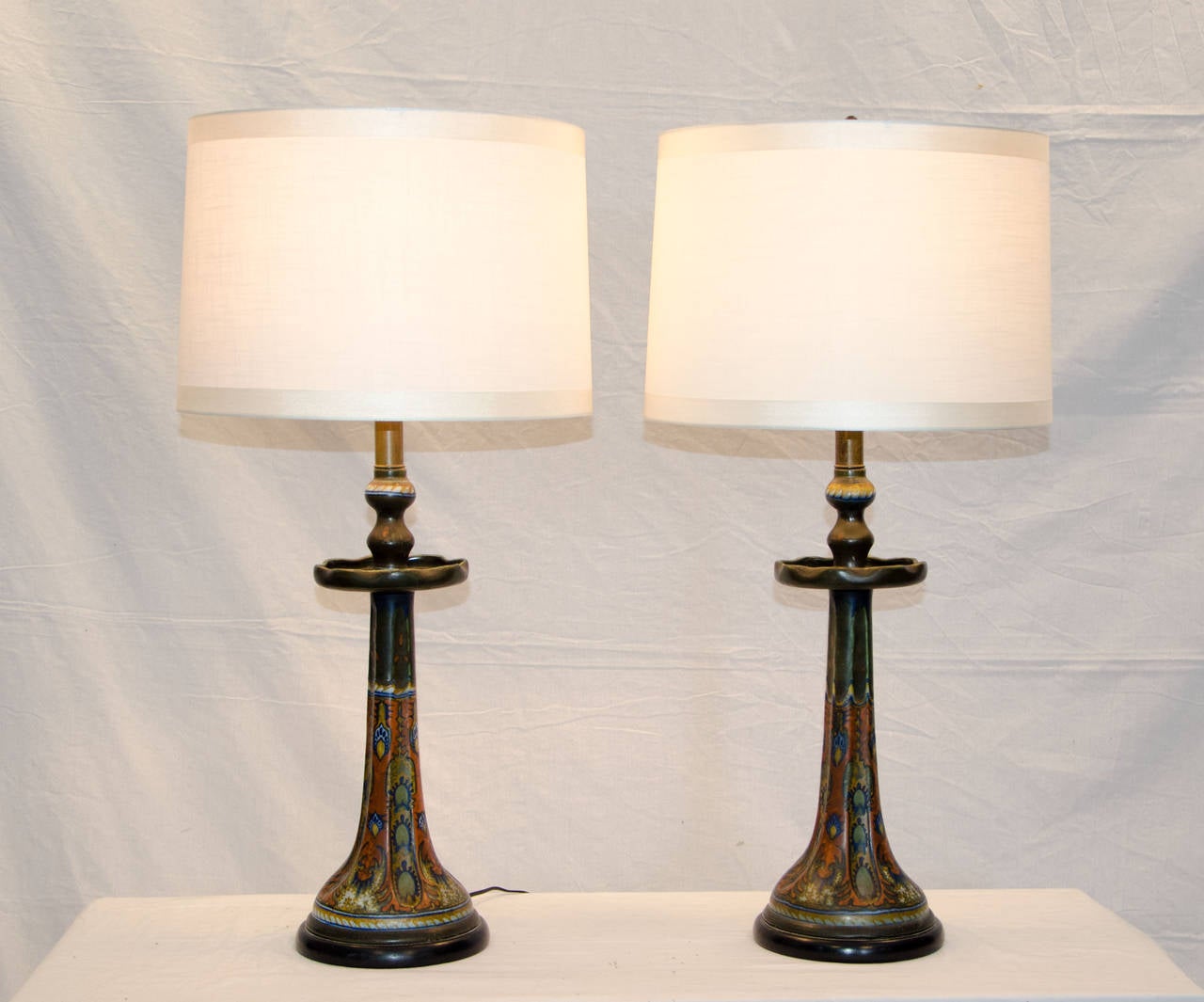 Hard to find pair of larger Gouda Pottery lamps, each base was hand-painted so they have slight differences but were originally purchased as a pair. 
There are many different colors. There are brass extensions between the pottery and light bulb