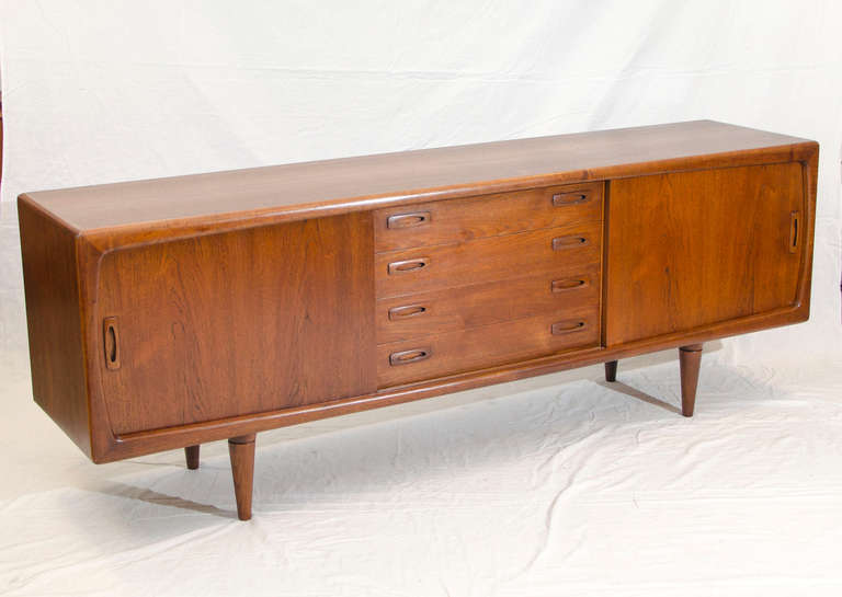 Nice Danish teak credenza with a curvier style. Two sliding doors on each side and a bank of four drawers in the center. Adjustable shelves in side compartments. Drawer handles inset into drawer fronts.