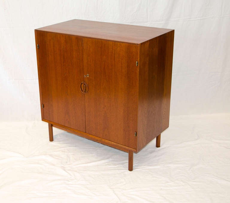 Iconic Danish teak storage cabinet designed by Peter Hvidt, displays his signature box joinery that connects the top and sides as well as the sculptural door pulls. The interior has one adjustable shelf and three shallow storage drawers. Originally