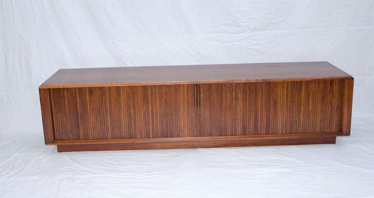 This walnut low credenza with tambour doors was manufactured by Barzilay. The back can be removed from center section for wiring space, one section has a pull out shelf originally for a stereo turntable. Perfect for low cabinet and large flat screen.