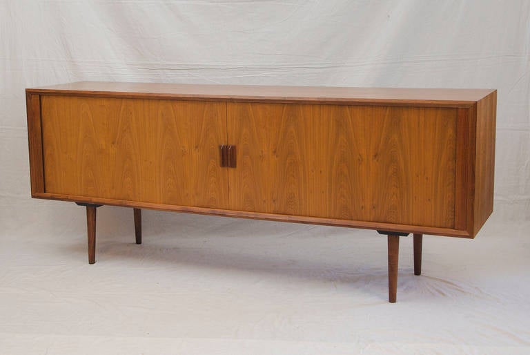 Nice walnut credenza with tambour doors , three adjustable shelves, and four shallow storage drawers in the interior. Tambour doors are accented with walnut pulls. Round tapered legs are also walnut. Tambour doors operate easily and smoothly.