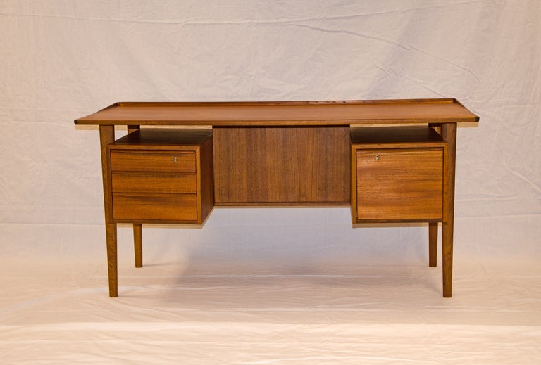Danish teak executive desk with lots of workspace. A raised gallery around three sides sets it apart and will prevent your papers from sliding off the work surface. Has a file drawer on one side as well as three drawers on the other. Will look good