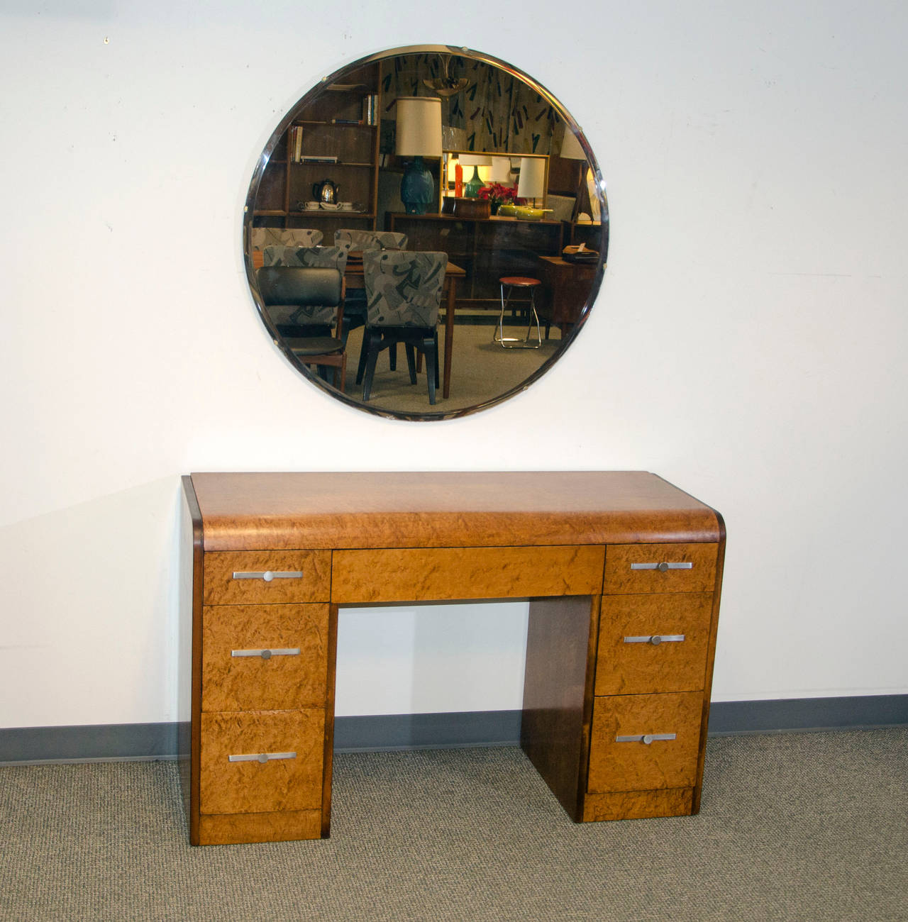 Nice bird's-eye maple vanity desk in the waterfall style. Has original stainless steel Art Deco drawer pulls. The round beveled mirror is a nice pairing. The mirror is 35 1/2