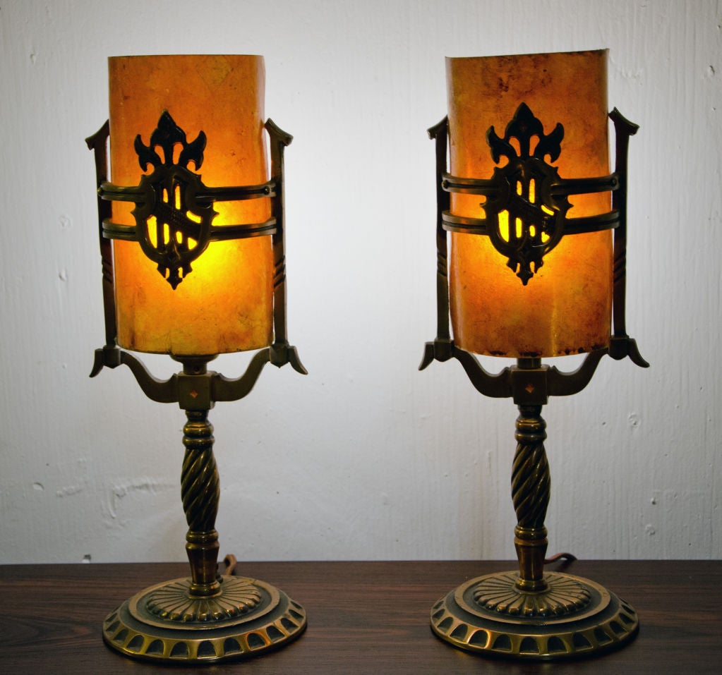 Nice pair of Art Deco lamps perfect for accenting a mantel or vanity. Made of Brass. Family crest type of decorative design with original Mica shades covering the bulbs. Each light has a on/off switch.