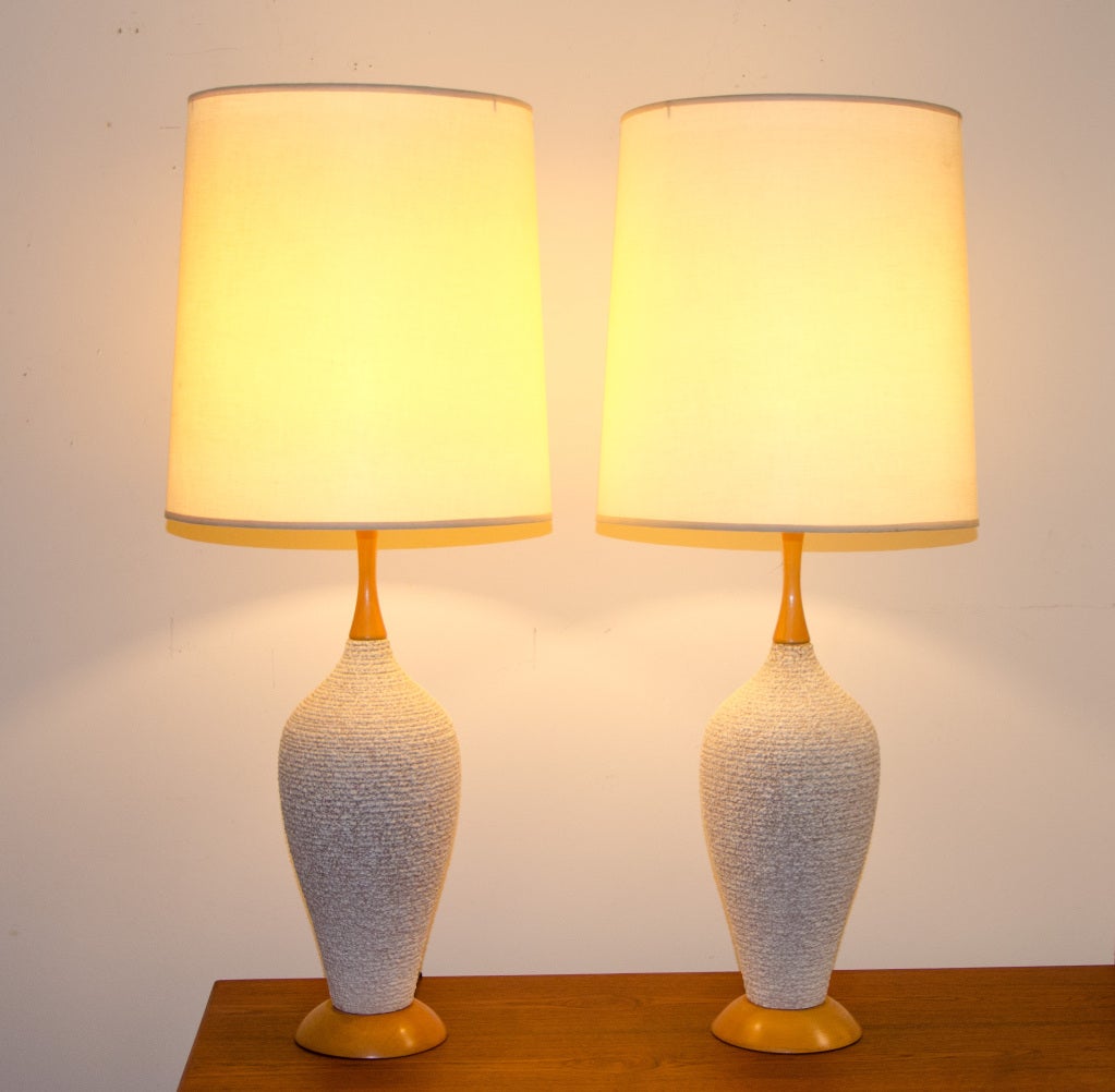Pair of mid century table lamps with ceramic bases that have a nice textured look. Blond wood has the original finish. Shades are appropriate size for bases. Ceramic section of base is 16" tall. Base is 5 1/2" diameter. Shade diameter is