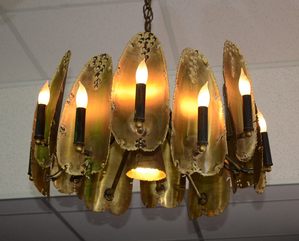 Unusual light fixture/chandelier in the brutalist  style by Tom Greene for Feldman Co.. Interesting pierced metal with flame style light bulbs in front. Twelve arms with center light. Elongated disks are attached to arms in a staggered pattern.