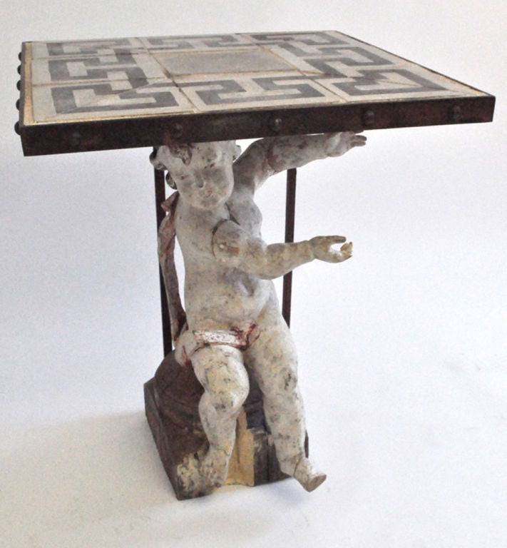 This very unique table.  The hand-carved wood angel is supported by metal base.  The table top is composed of black and white Italian tiles with a Greek key design, framed by a metal base and iron bolts.