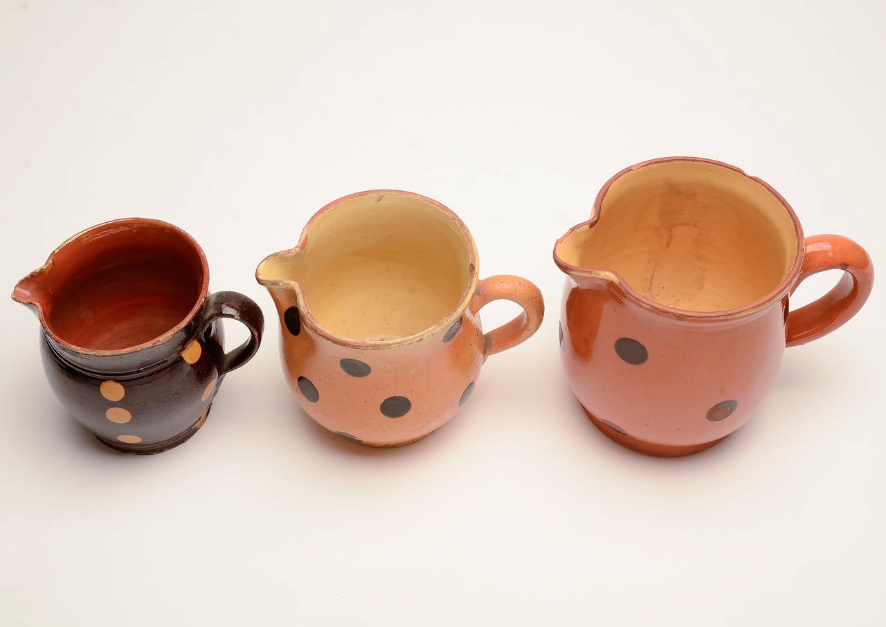 Three jaspe pitchers typical of the collectible designs of this rustic terra cotta French pottery. The pitcher on the left with orange dots on brown measures 3 3/4