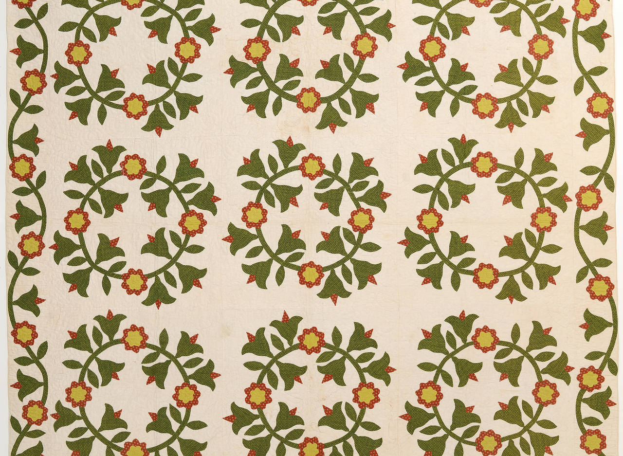 This Classic tulip wreaths quilt is different from the usual in that it is not red and green. Instead of red, it has a terra cotta or brick color lightened with yellow floral centers. The border beautifully continues the applique of the body of the