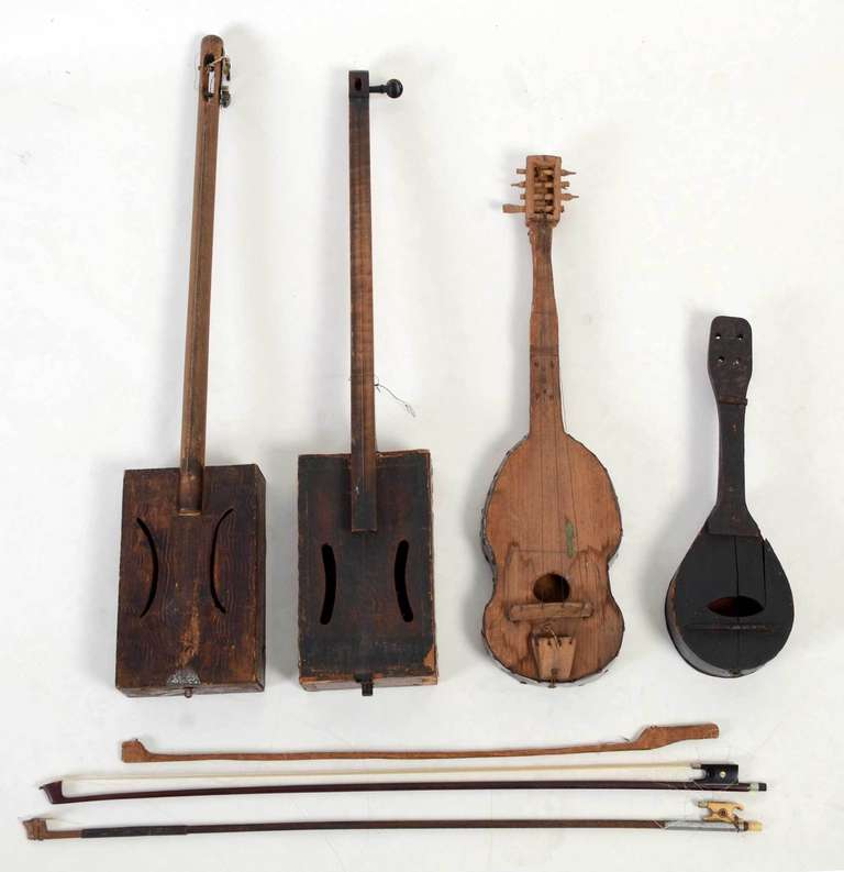 Four homemade musical instruments are made from a variety of recycled parts. The bodies of all but the fiddle are cigar boxes; the fiddle is banded with previously used metal. They were likely meant as actual instruments to be played but would make