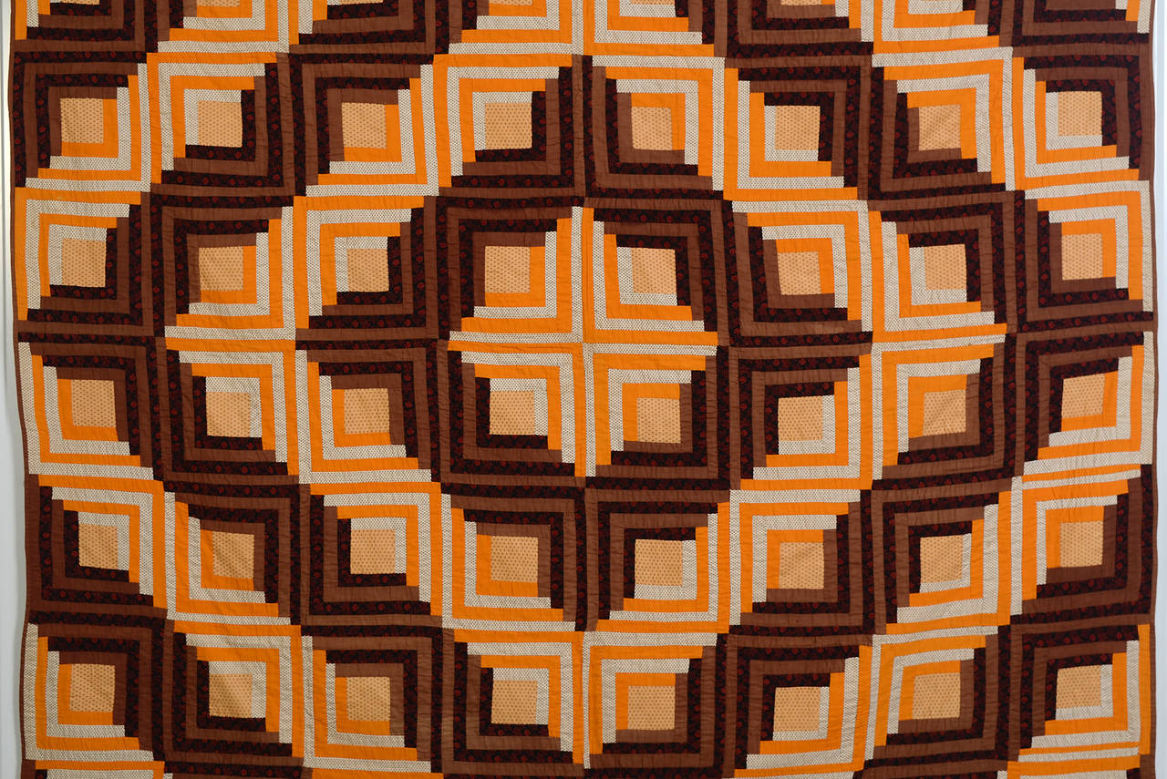 This Classic barn raising log cabin quilt is done with an unusual color palette. Solid and printed oranges and browns are beautifully combined. The quilt is in excellent condition. Measurements are 82