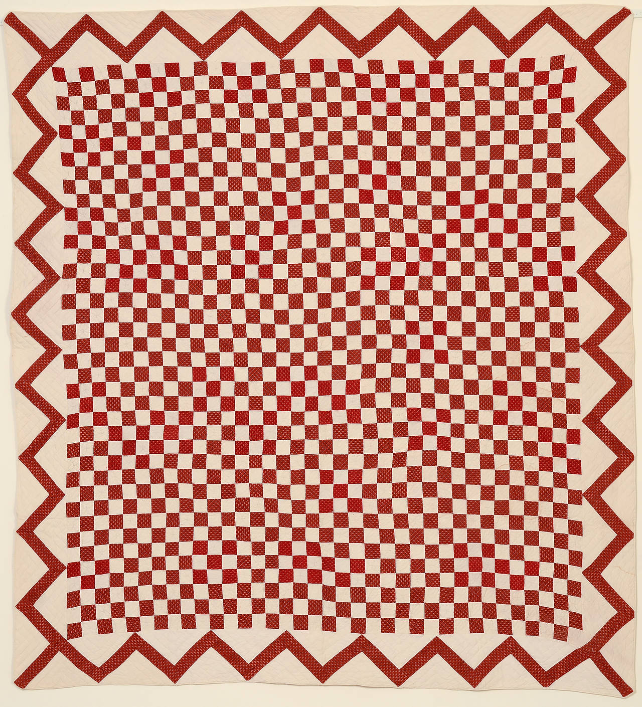 Several features elevate this one-patch quilt beyond the simple pattern that it is. Subtle variation in the printed red fabrics create an effective shading. Abutting the blocks gives a nice positive or negative effect and finally, the strong zigzag