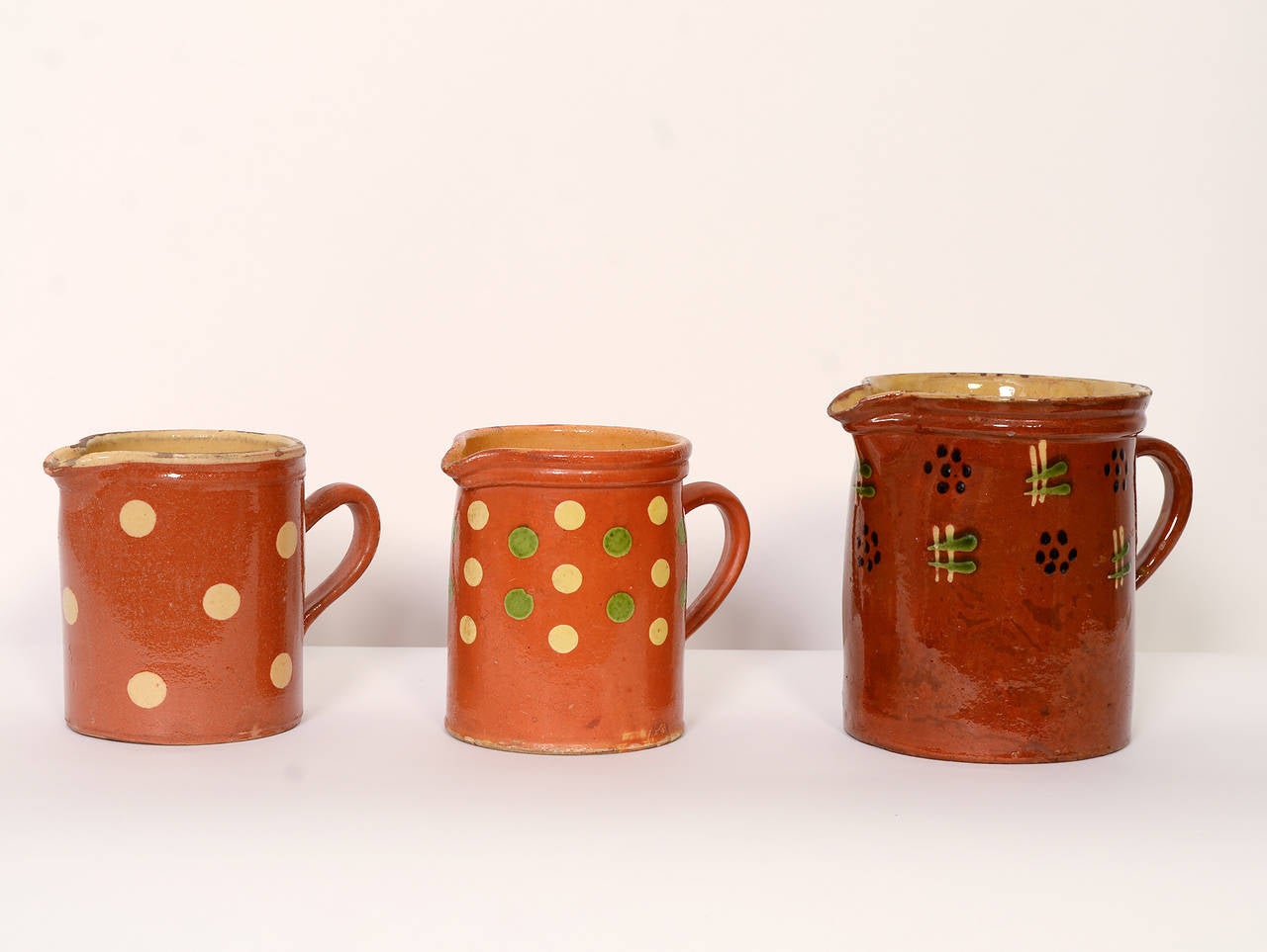 Three jaspe pitchers typical of the collectible designs of this rustic terra cotta French pottery. The pitcher on the left with yellow dots measures 5 5/8